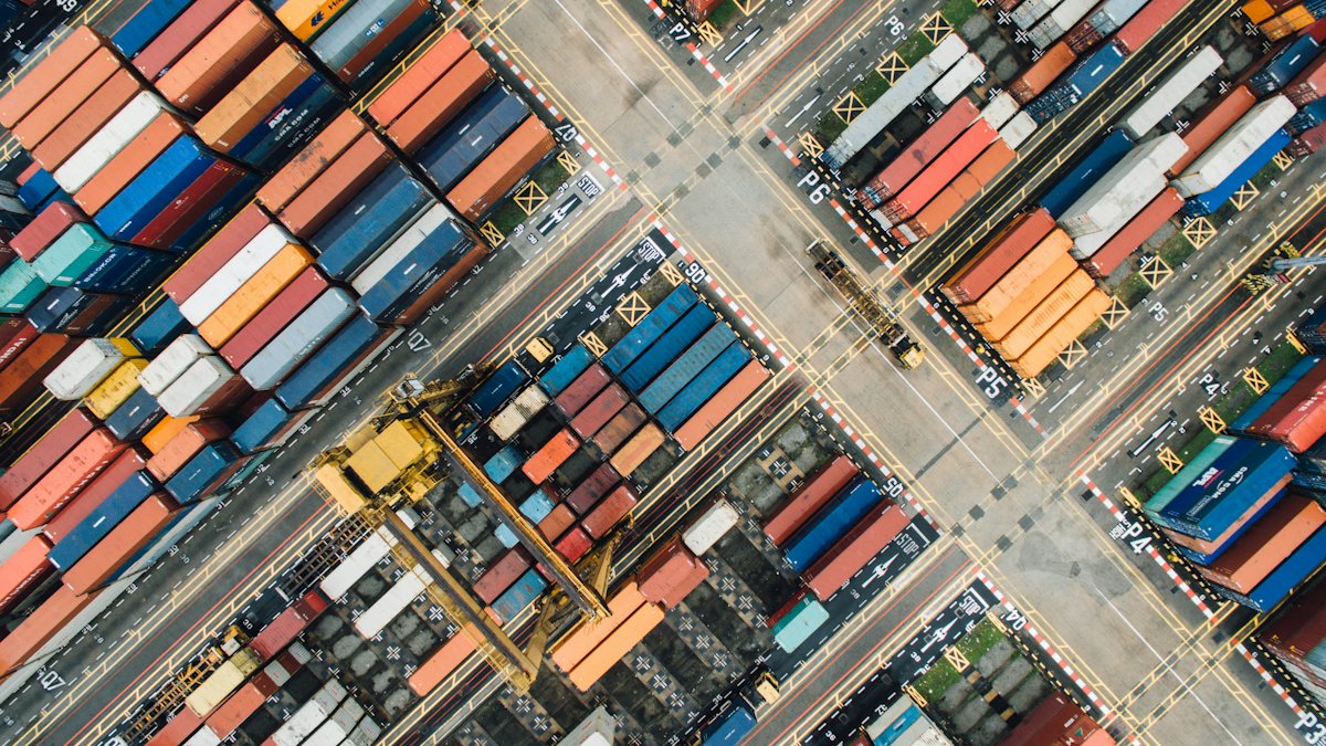 An aerial view of a shipping container yard, containers stacked in coloured blocks