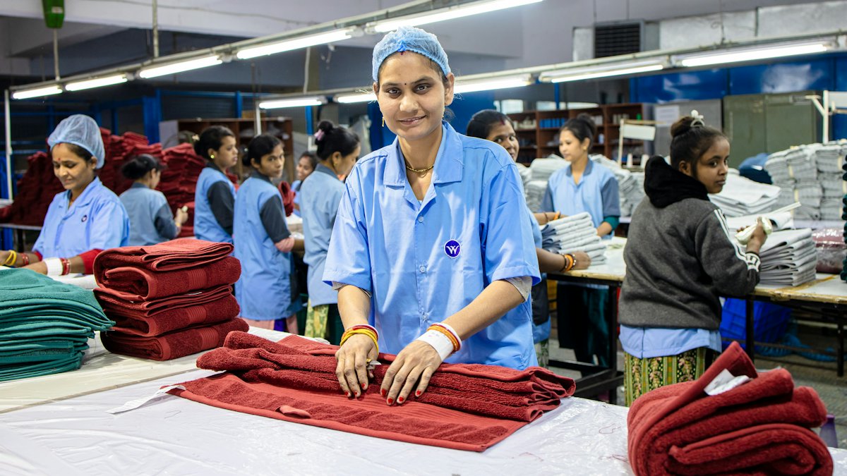 A worker folding finished red towels at a packing table, with the rest of the line working behind her