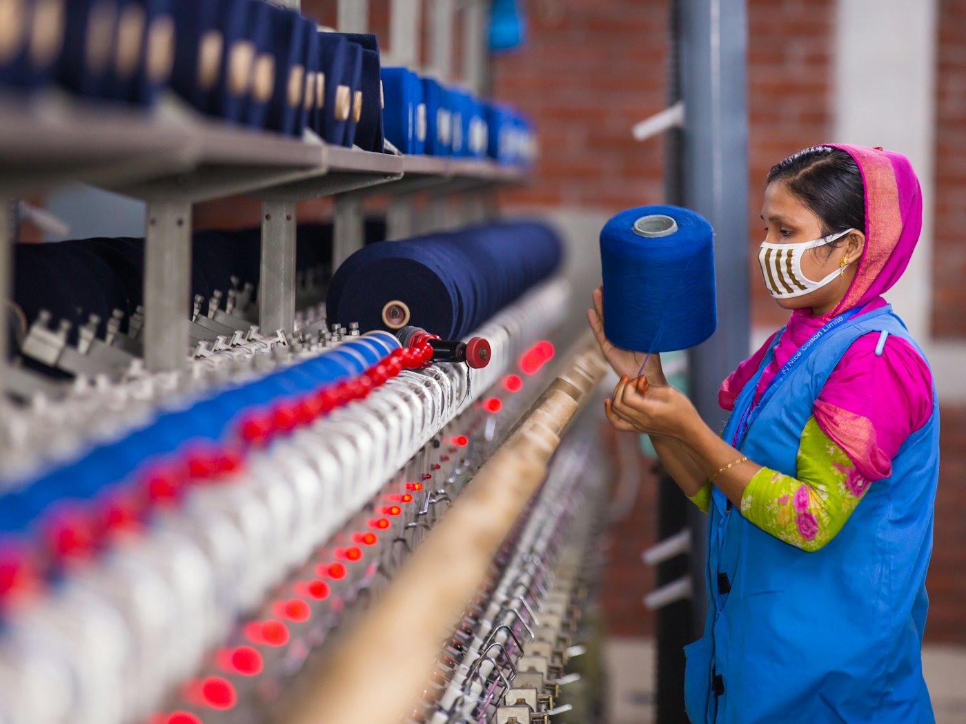 A spinning mill worker holding a cone of blue yarn beside a winding machine